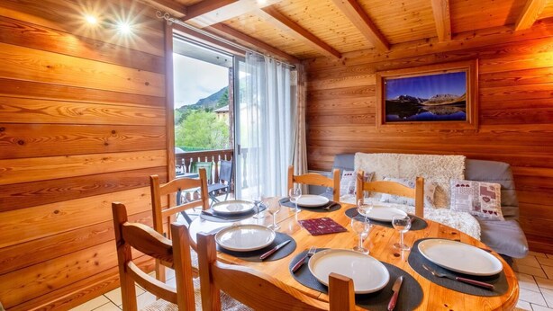 A wooden cabin with a dining area set for four, a sofa, and a scenic view through a large window. - L'oree DU Bois - Arole (VAL CENIS)