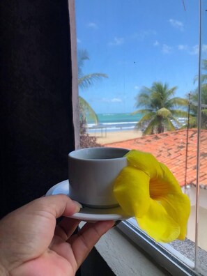 A hand holding a gray cup with a yellow flower. - Pousada Genipabu Praia (Extremoz)