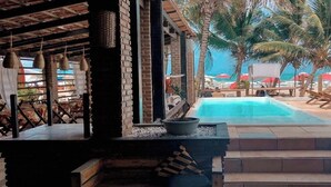 Ein Poolbereich mit Blick auf den Strand, Liegestühlen und Palmen.