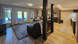 Amplia sala de estar con un sofá grande, una mesa de centro y una alfombra. Hay puertas corredizas de vidrio que dan a un patio con vista al lago.