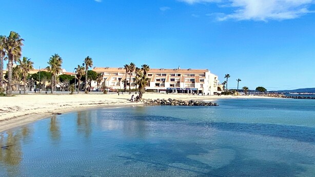 Ein Hotel direkt am Strand mit Sand, Palmen und klarem, blauem Wasser.