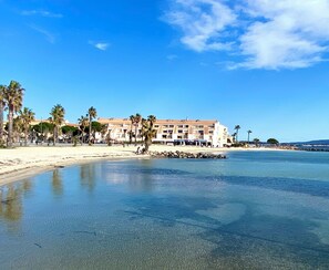Ein Hotel direkt am Strand mit Sand, Palmen und klarem, blauem Wasser.