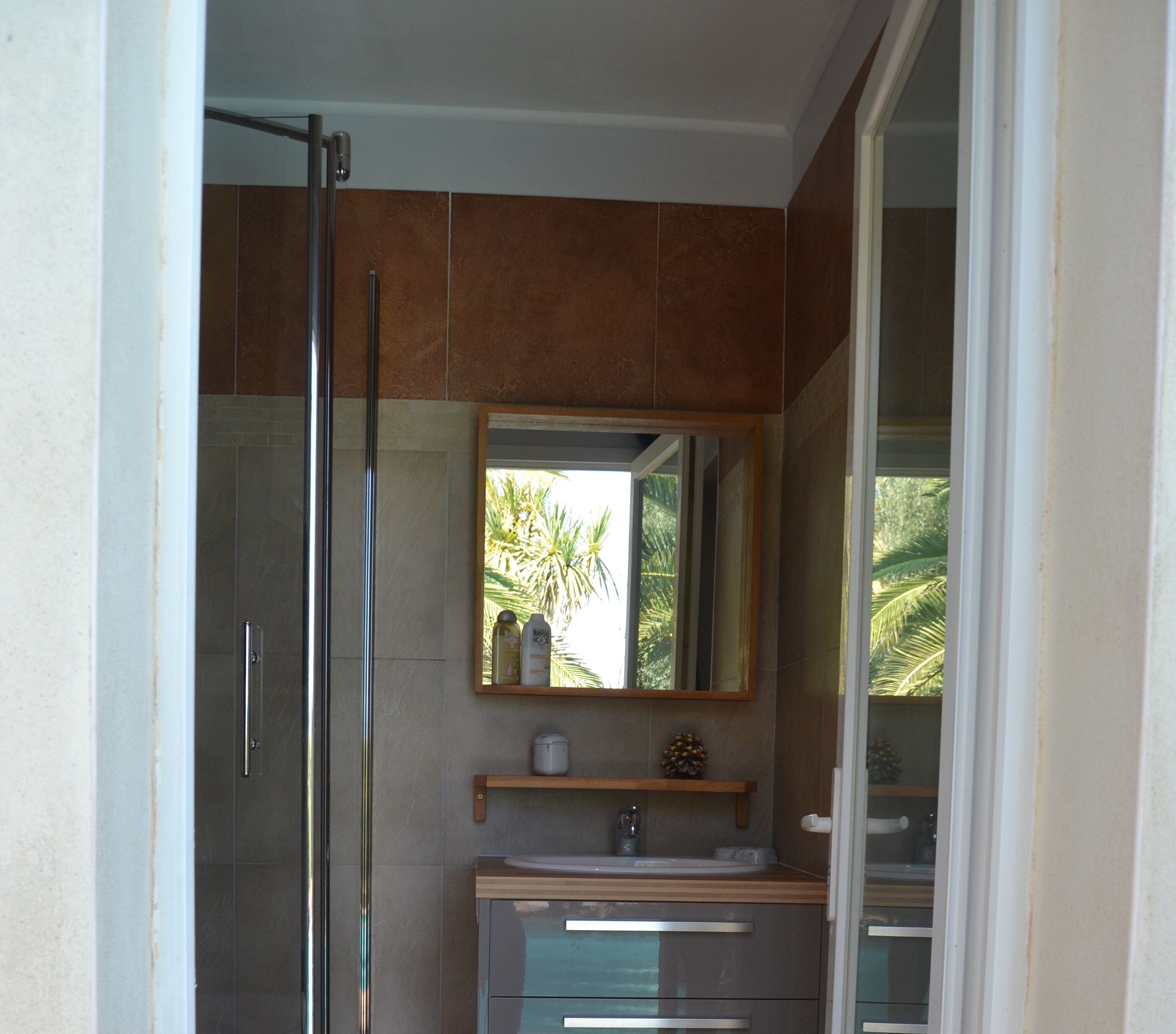 A bathroom with a glass shower door, a sink with a mirror above it, and a shelf with toiletries.