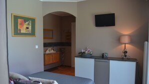 Ein Schlafzimmer mit einem Bett, einem Schreibtisch mit Lampe, einem Fernseher und einem durch einen Bogen sichtbaren Badezimmer.