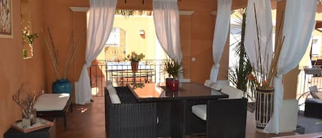 An outdoor dining area with wicker furniture, white curtains, and potted plants.
