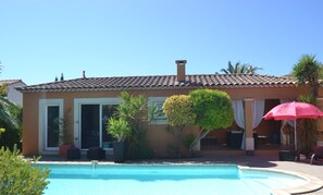 Un espace aménagé au bord de la piscine, doté d’un toit carrelé, d’une piscine et d’un bâtiment avec une porte et des fenêtres.