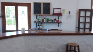 A bar area with a counter, stools, a shelf with bottles, a chalkboard menu, and a window with a view of greenery. - Eco Art Hotel (Peralejos de las Truchas)