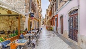 A narrow street lined with cafes and restaurants, featuring outdoor seating with tables and chairs, stone buildings, and a clear sky. - 1 bedroom cozy apartment in Pula (Pula)
