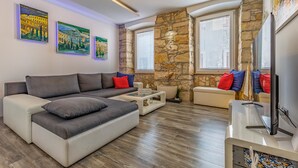 A modern living room with a sectional sofa, a coffee table, and a TV. There are paintings on the wall and a stone wall feature. - 1 bedroom cozy apartment in Pula (Pula)