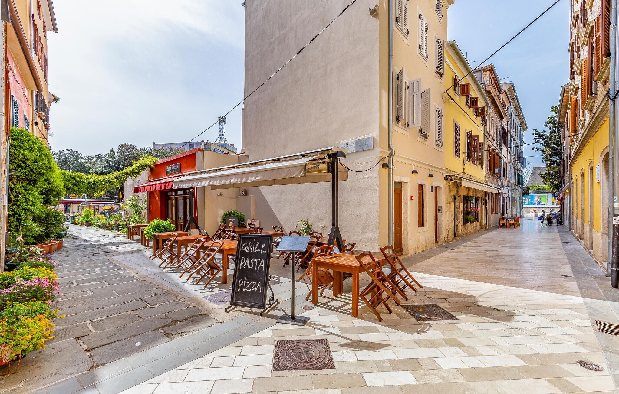 An outdoor café with tables and chairs, a chalkboard menu, and a cobblestone street.