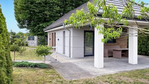 A modern house with a covered patio, a small garden, and a stone wall in the background. - Gorgeous home in Drogoradz (Drogoradz)