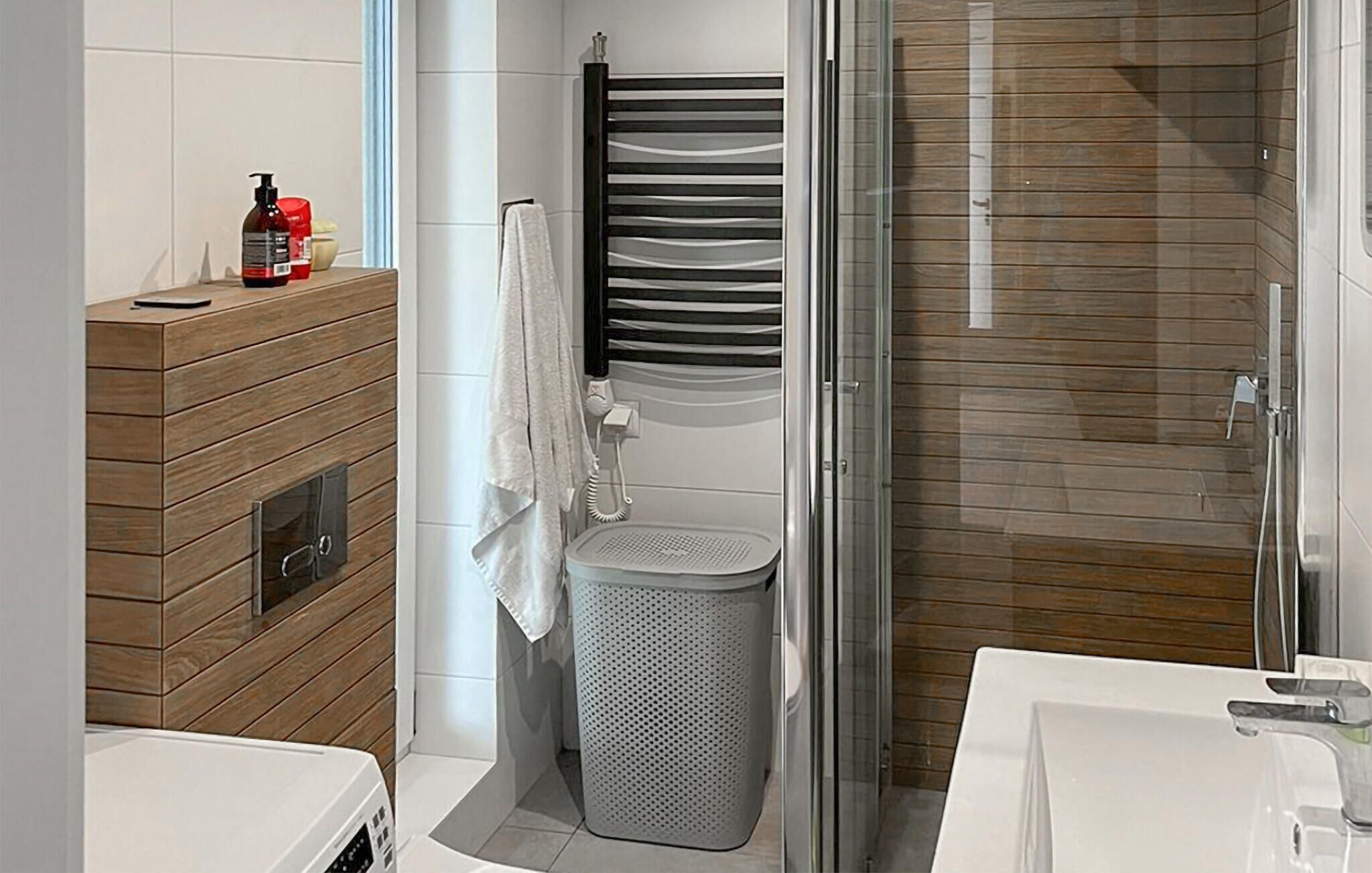 Une salle de bain moderne avec un meuble-lavabo en bois, une douche dotée d’une porte en verre et des toilettes équipées d’un panier à déchets perforé.