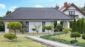 Une maison moderne à deux étages, avec un toit gris, des murs extérieurs blancs et un porche abrité.