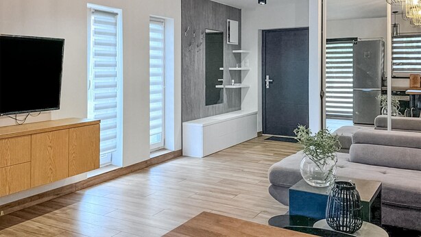 A modern living room with a flat-screen TV, wooden flooring, a grey sofa, and a coffee table with decorative items. - Gorgeous home in Drogoradz (Drogoradz)