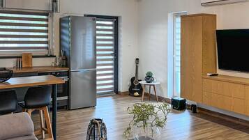 A modern kitchen with a built-in refrigerator, a dining area with a wooden table and chairs, a guitar, and a television on a wooden cabinet.
