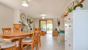 A spacious dining area with a wooden table and chairs, a kitchen with a brick backsplash, and a white cabinet with decorative knobs.