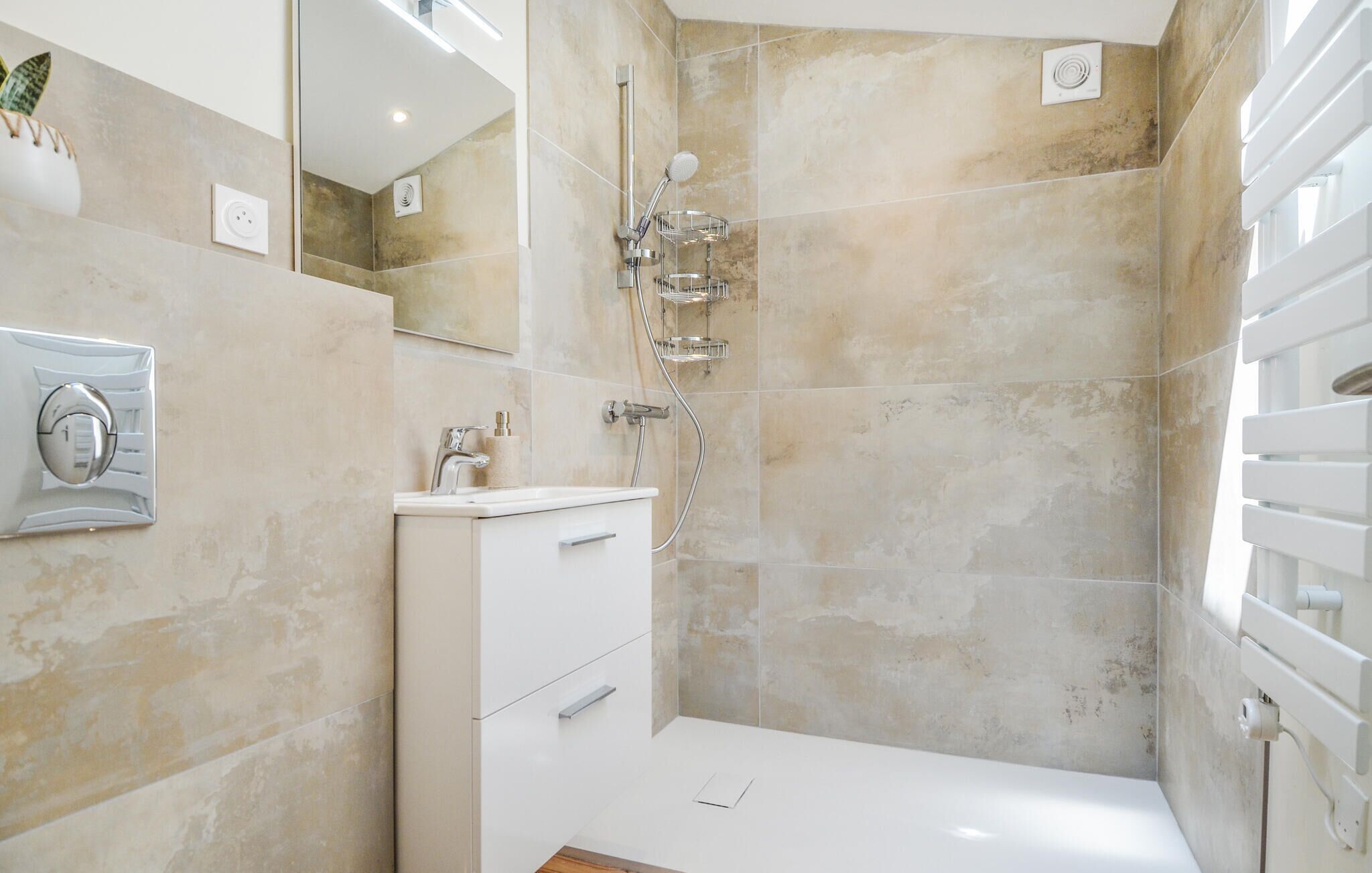 A modern bathroom with beige tiles, a white sink, a mirror, and a shower with a handheld showerhead.