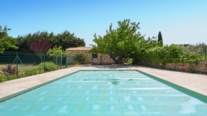 A swimming pool with a tiled deck, surrounded by a stone wall and greenery.