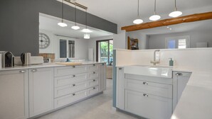 A modern kitchen with white cabinetry, a central island, pendant lighting, and a large window.