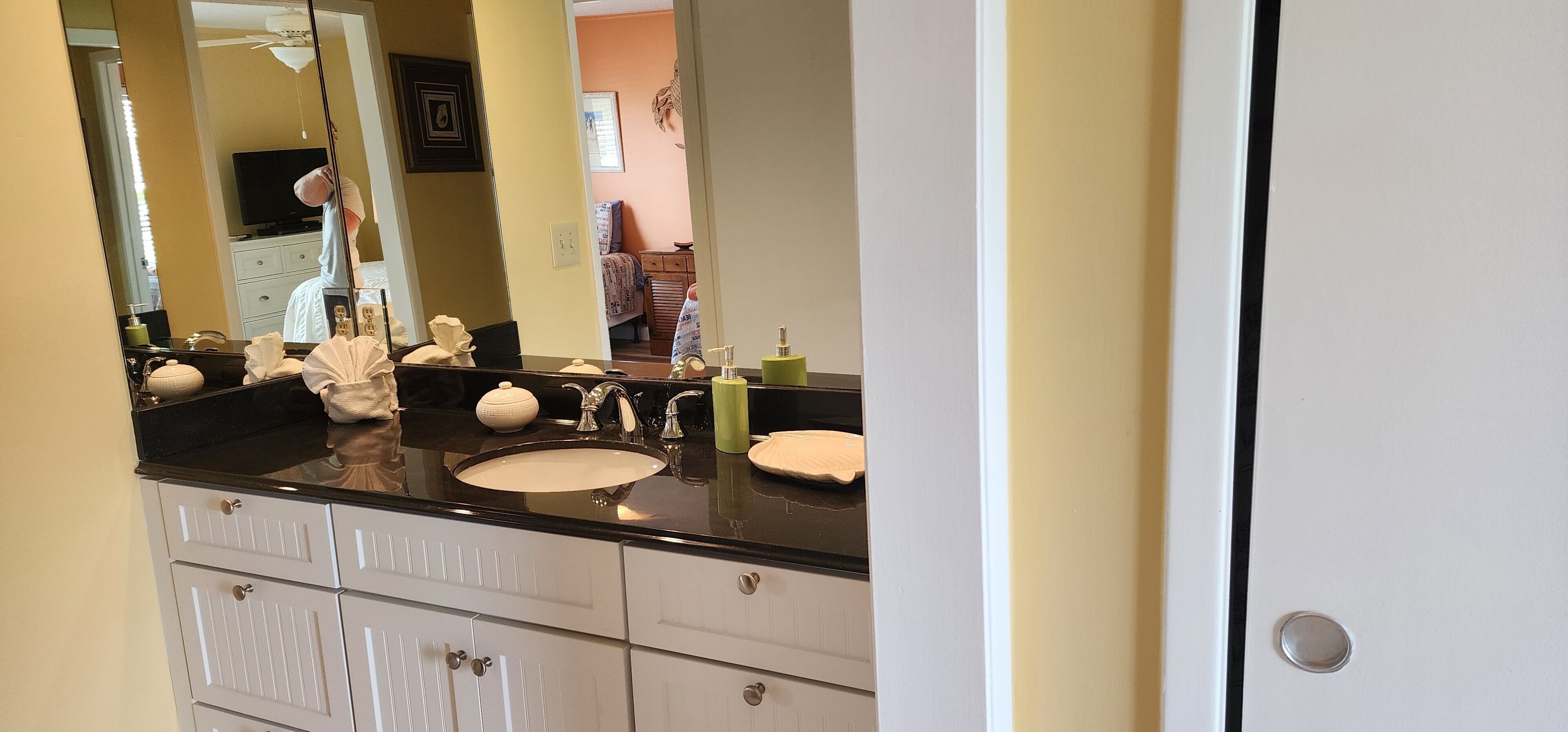 Un baño con un espejo grande, una encimera negra, un lavabo blanco y un mueble con cajones.