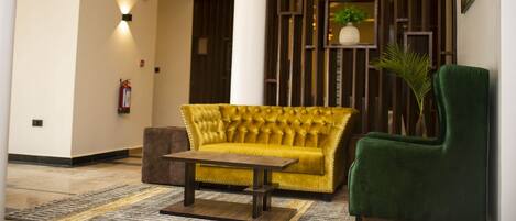 Un vestíbulo con un sofá amarillo, un sillón verde y una mesa de centro de madera.