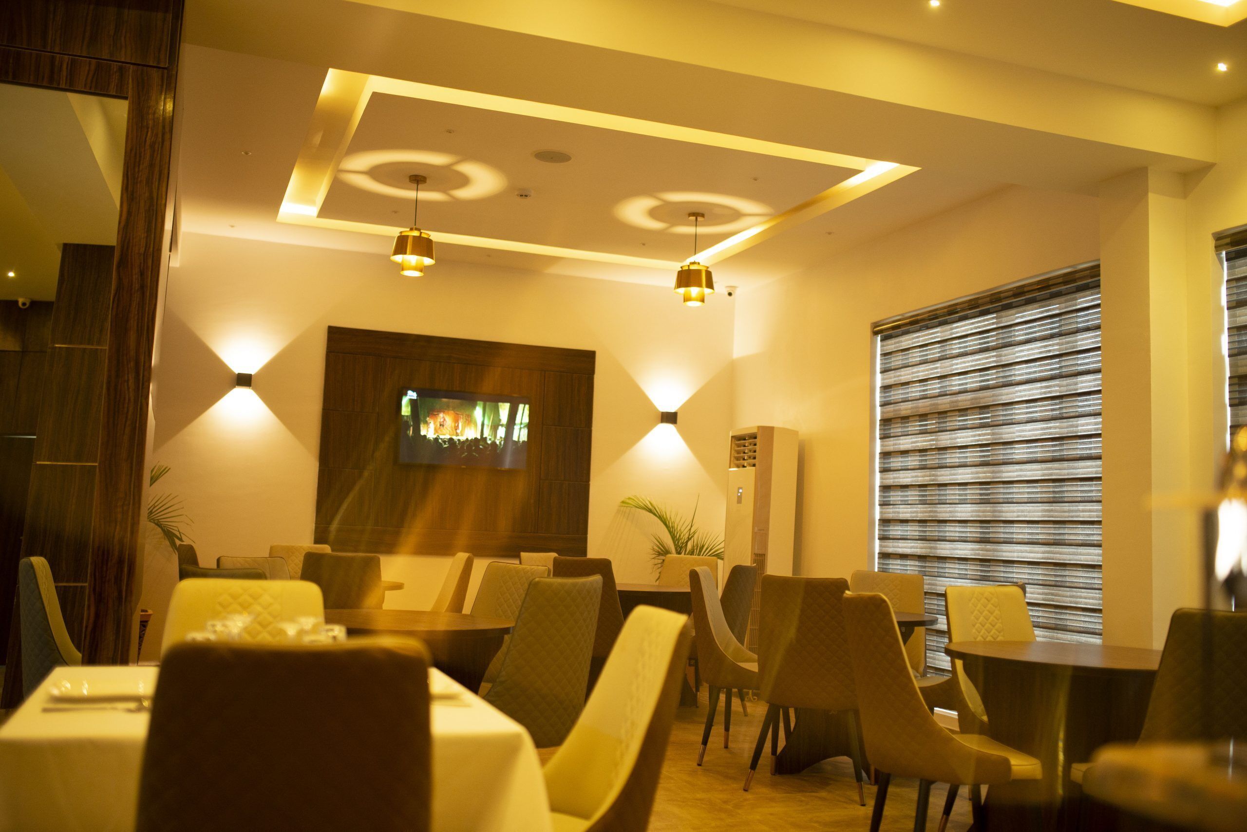 A restaurant with tables and chairs, a television screen, and pendant lighting.