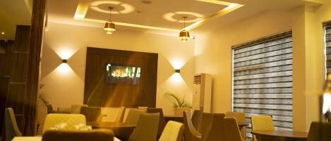 A restaurant with tables and chairs, a television screen, and pendant lighting.