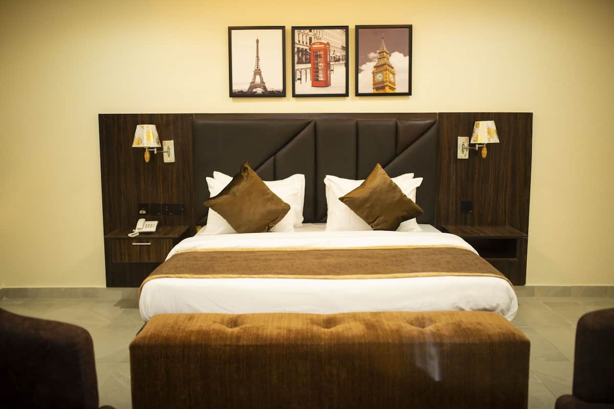 A hotel room with a large bed, brown and white bedding, a wooden headboard, two bedside tables with lamps, and three framed pictures on the wall.