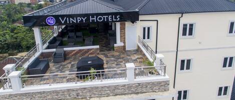 Un edificio de Vinpy Hotels con un patio en la azotea que cuenta con mobiliario exterior y una zona de estar cubierta.