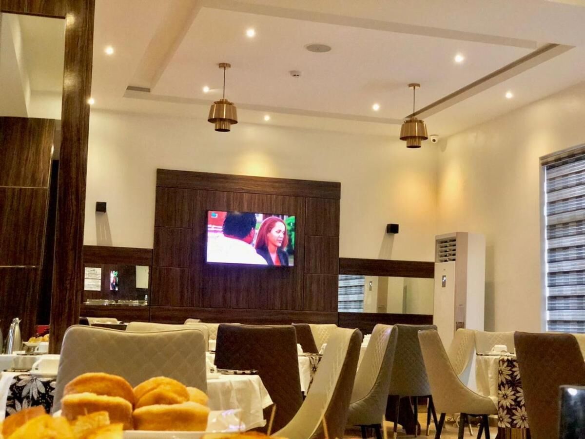 A restaurant with a TV mounted on the wall, tables with chairs, and a ceiling with recessed lighting.