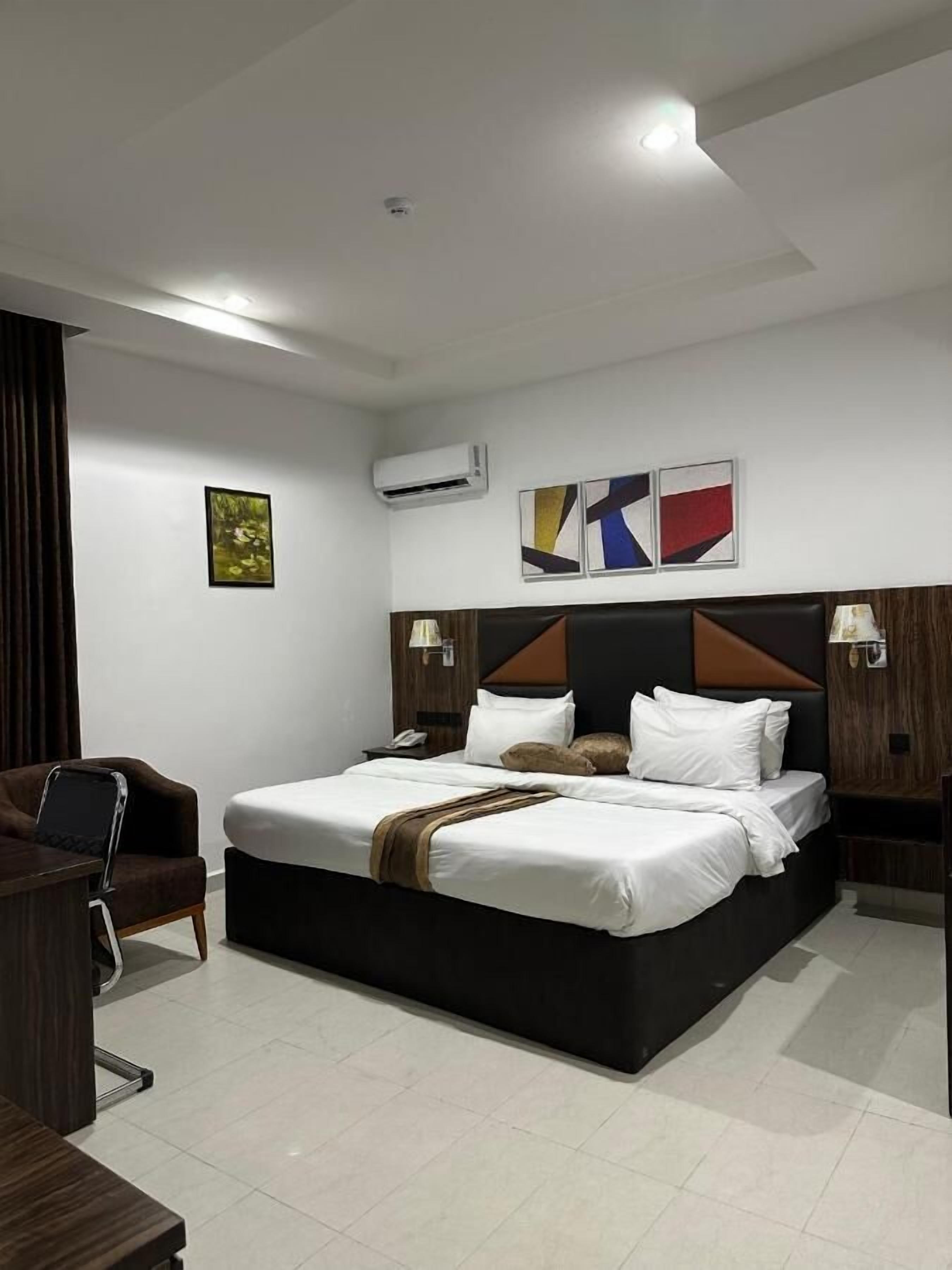 A modern hotel room with a large bed, a desk, and a chair. There are three wall-mounted air conditioning units and two wall-mounted lamps.