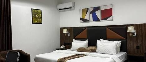 A modern hotel room with a large bed, a desk, and a chair. There are three wall-mounted air conditioning units and two wall-mounted lamps.