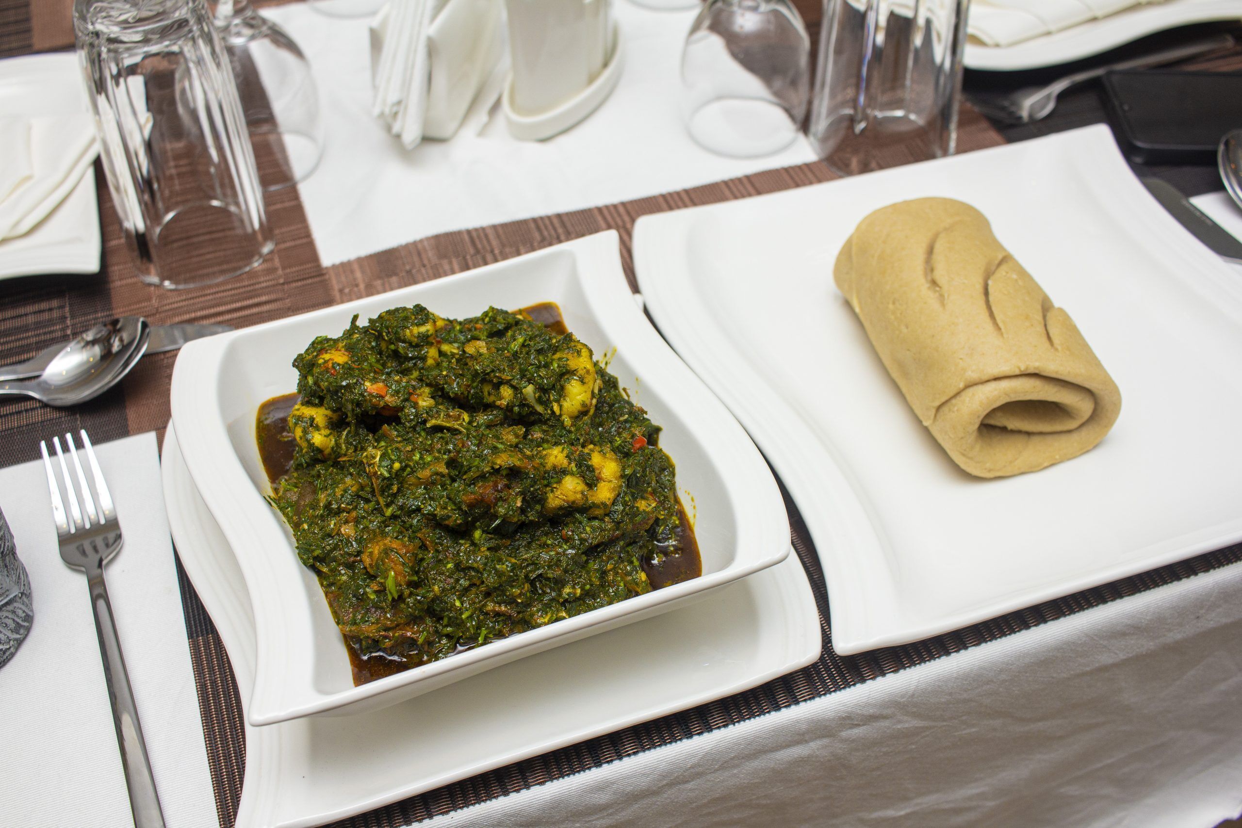 A meal with a green vegetable dish and a rolled flatbread on a white plate, set on a table with a placemat.