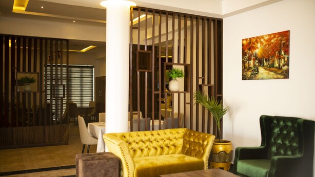 A modern living room with a yellow sofa, a green armchair, and a wooden coffee table. - Vimpy Hotel Uyo (Uyo)
