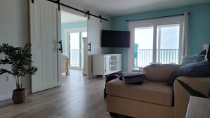 Una sala de estar con sofá, televisor, puerta corrediza y vistas al exterior.