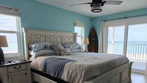 Un dormitorio con cama, mesita de noche, lámpara y vista al océano a través de un ventanal grande.