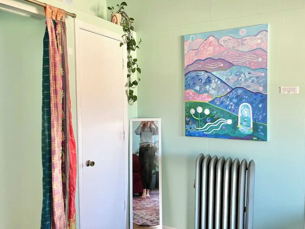 Um quarto com uma porta, um radiador e um quadro colorido na parede.