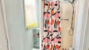 Ein Badezimmer mit Duschvorhang mit Obstmuster, einem Handtuchhalter mit gelbem Handtuch und einer Ablage für Toilettenartikel.