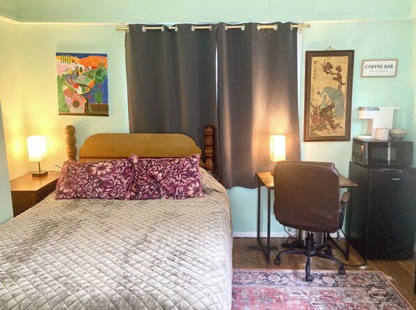 Un dormitorio con cama, dos lámparas de noche, un escritorio con silla, barra de café y obras de arte en las paredes.