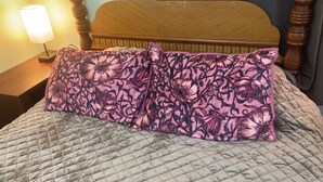 Ein Bett mit einer gesteppten, grauen Decke und einem floralen Kissen.