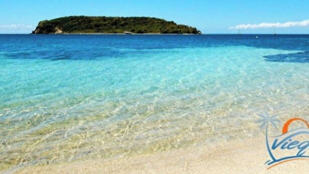 A beach with clear turquoise water and a small island in the distance.