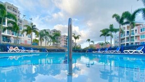 A swimming pool with lounge chairs and palm trees, surrounded by multi-story buildings.