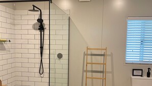 Une salle de bain avec un carrelage noir et blanc, une douche avec un tuyau noir, une chaise en bois et des toilettes sur lesquelles est affiché un panneau.