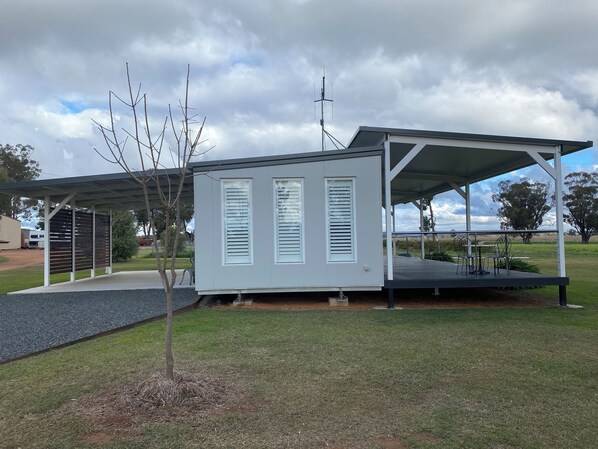 Un bâtiment moderne, de plain-pied, doté d’un espace extérieur abrité avec des sièges et d’un petit arbre à l’avant.