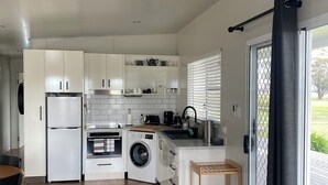 Une cuisine moderne avec des meubles blancs, un four encastré, un lave-linge et un coin repas comprenant une table et des chaises.