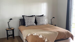 Une chambre à coucher comprenant un lit, deux tables de chevet, un ventilateur de plafond, un appareil de climatisation et une fenêtre avec des rideaux.