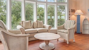 Una habitación con un ventanal grande, una mesa redonda de madera, un sofá color beige y una silla de mimbre.