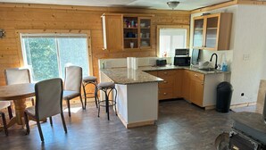 A modern kitchen with wooden cabinets, a granite countertop, and a dining area with chairs. - Off Grid Cabin With WIFI! Surrounded by hiking trails, beautiful scenery (Lowman)