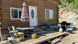 A wooden cabin with a porch, a table with chairs, a grill, and a door with a window. - Off Grid Cabin With WIFI! Surrounded by hiking trails, beautiful scenery (Lowman)