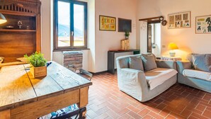 A cozy living room with a wooden table, two sofas, a large window, and a brick floor. - Tommaso by Interhome (Gravedona)